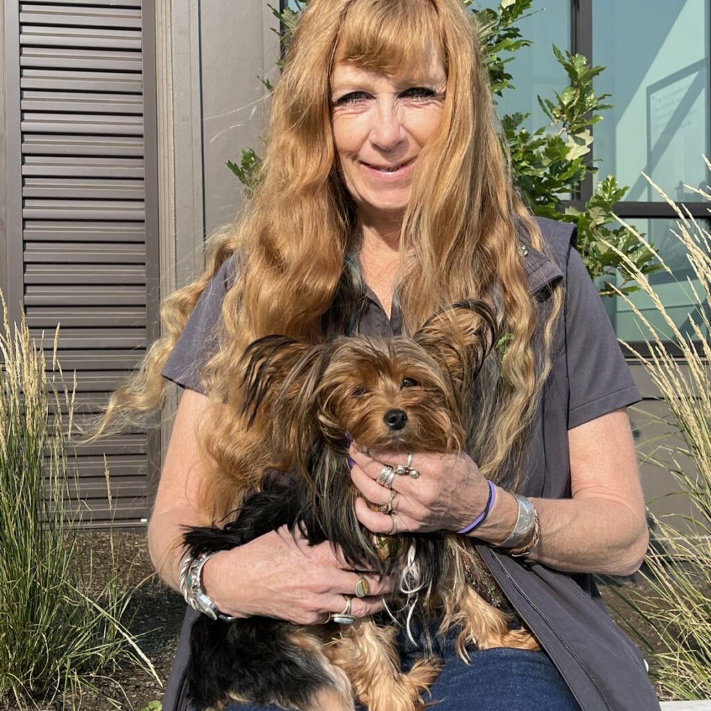 Terry Johnson sitting outside a house holding her small dog on her lap